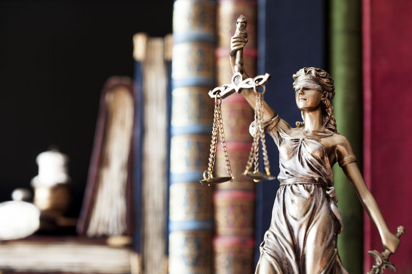 Estatua de la justicia con balanza ante una estantería de libros de derecho
